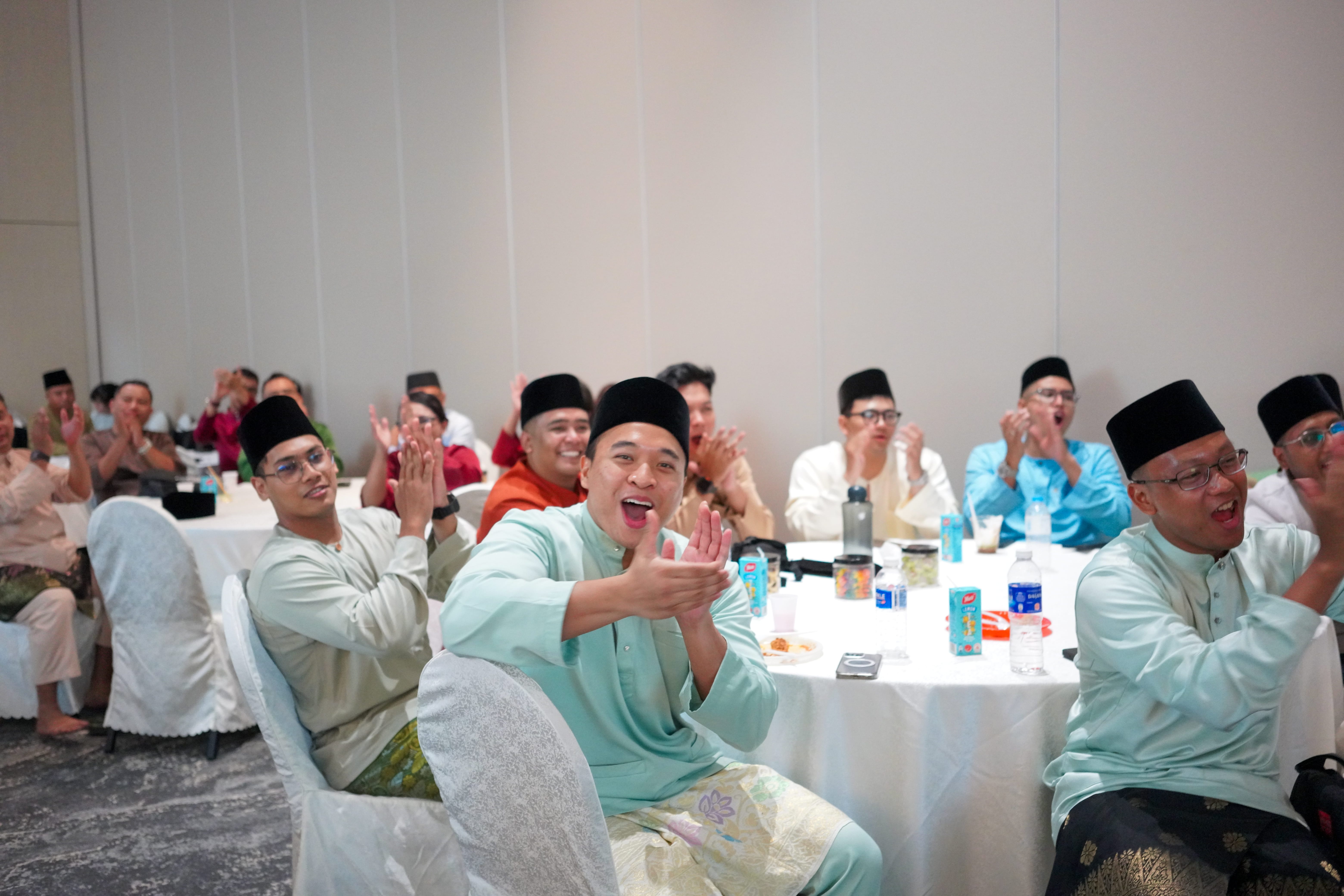Guests in traditional attire applauding and cheering from their tables during a lively stage performance.